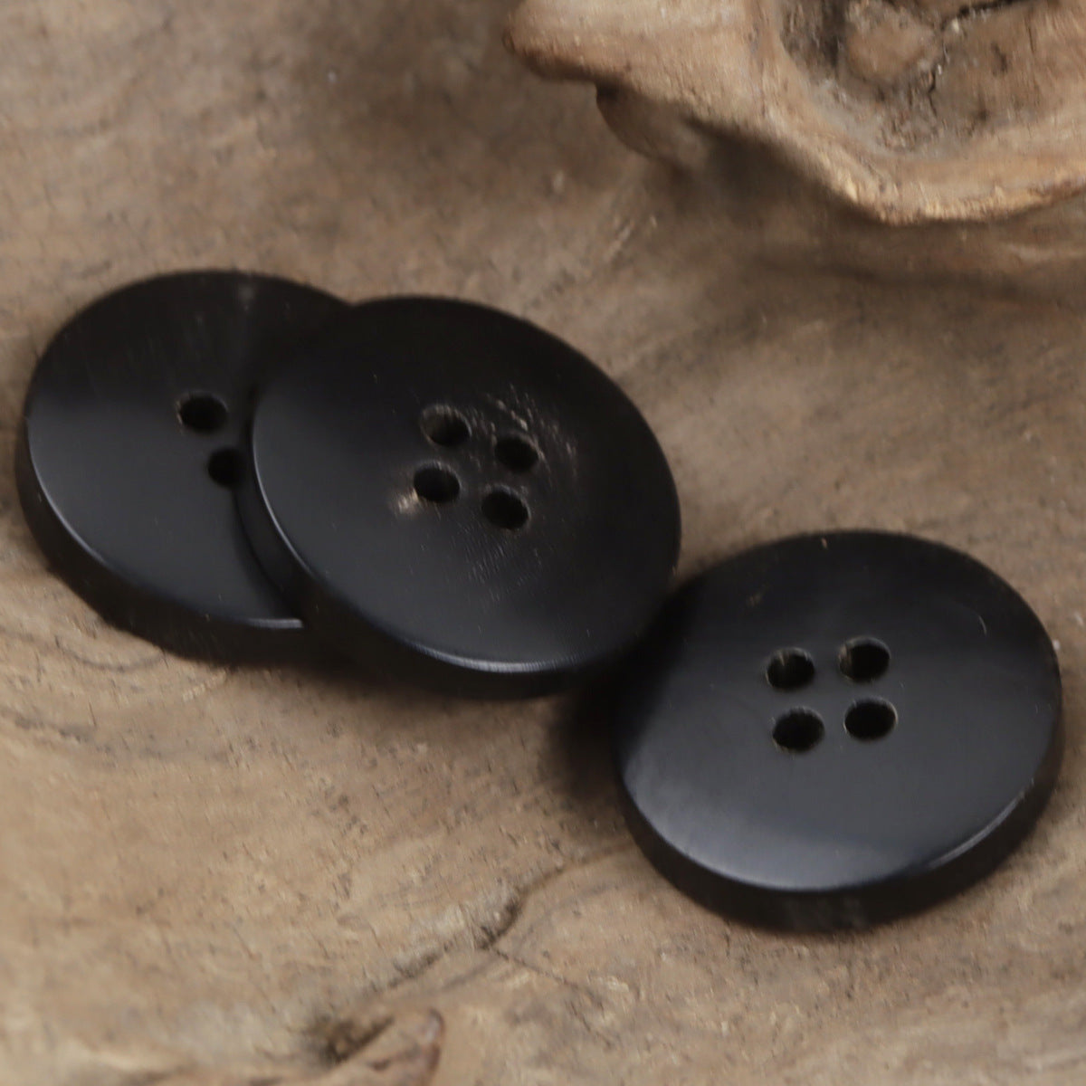 Two dark horn bowl buttons with four holes, gold-edged rim, angled overlap