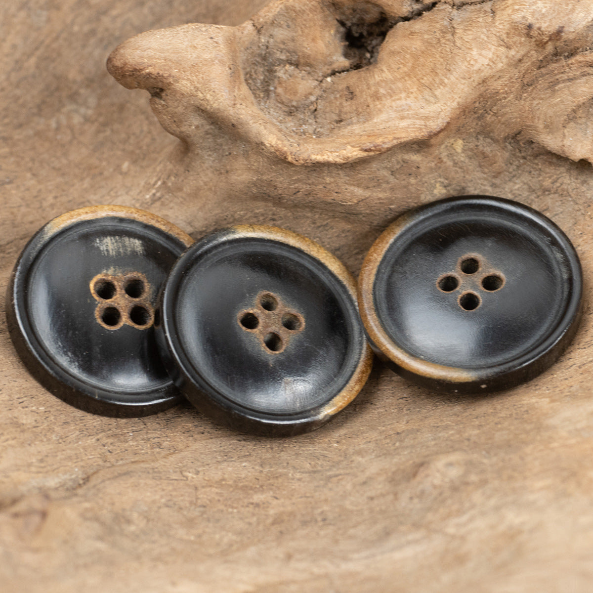 Four black four-hole clothing buttons with brown natural horn rim detailing