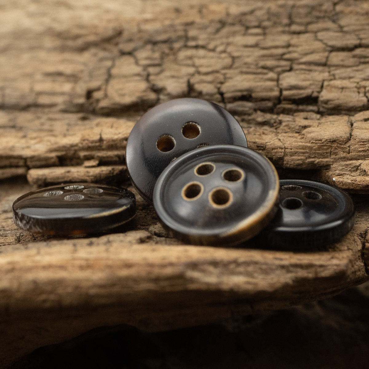 Black 4-hole shirt buttons with burnt-edge rim, on wooden surface