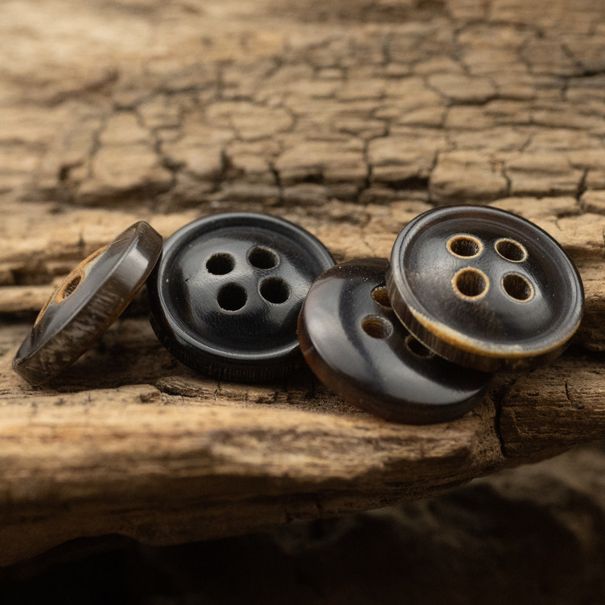 Set of black 4-hole horn shirt buttons with burnt-edge detail, laid on wood