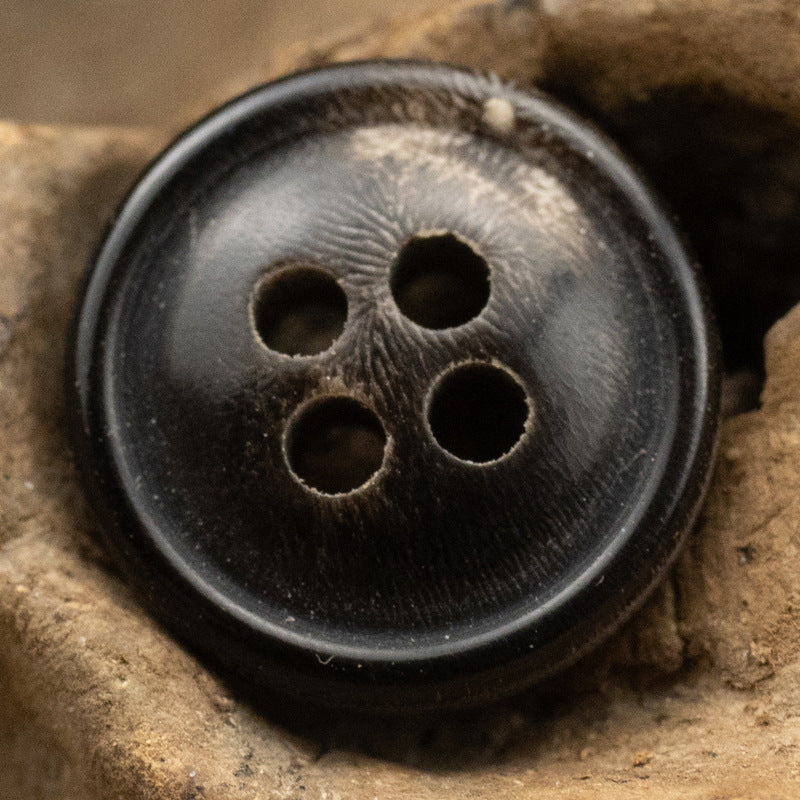 Black 4-hole horn button close-up with textured face and burnt-edge rim