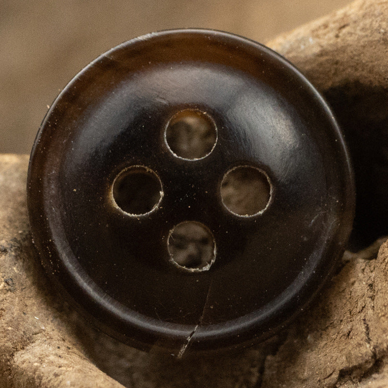 Worn black 4-hole horn button with burnt-edge rim and four eyelets