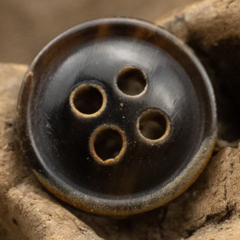 Close-up: black 4-hole horn shirt button with burnt-edge rim