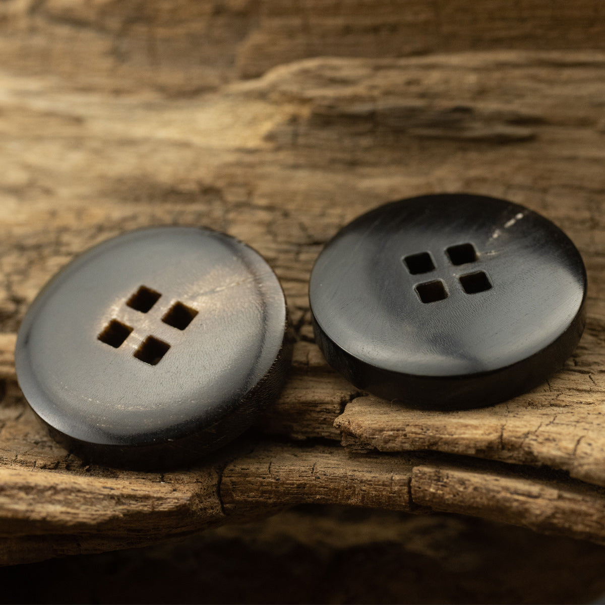 Black horn button with square holes, front view on wood