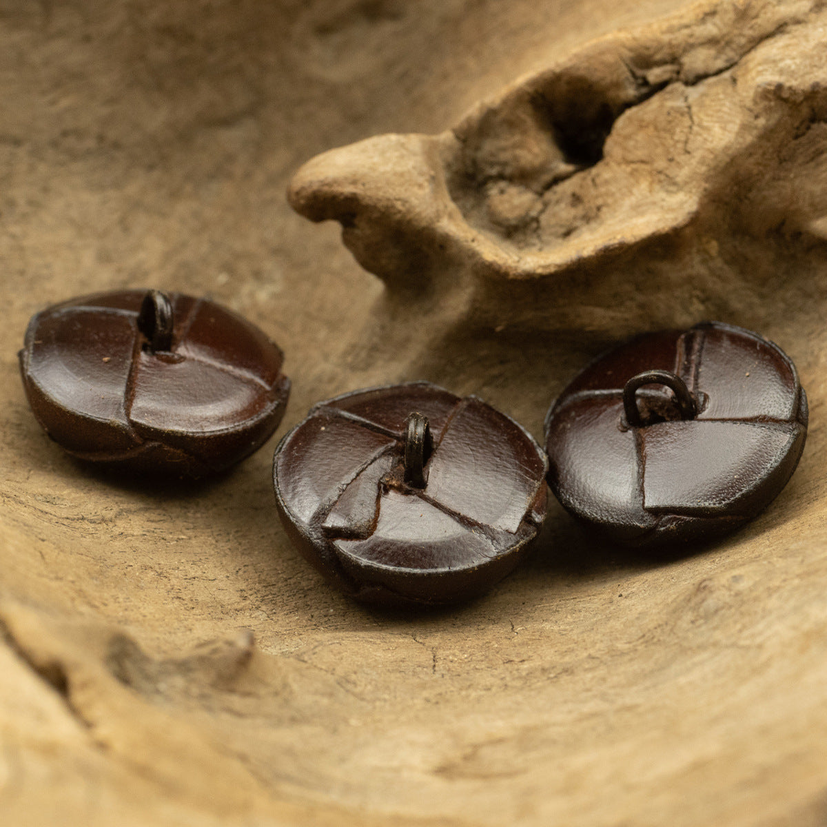 Round dark brown leather button pair with stitched panel seams and loop backs