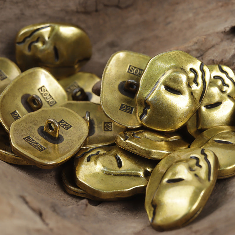 Gold/antique bronze face-motif buttons with metal shanks; engraved markings on the backs