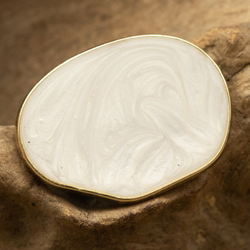 White irregular oval pearl-look glass button with glossy swirl pattern and gold edge.