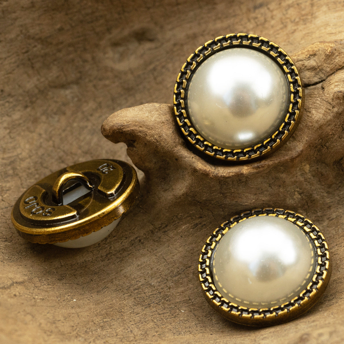 Pearl button pair with bronze stitched-style lace border; one shank back visible