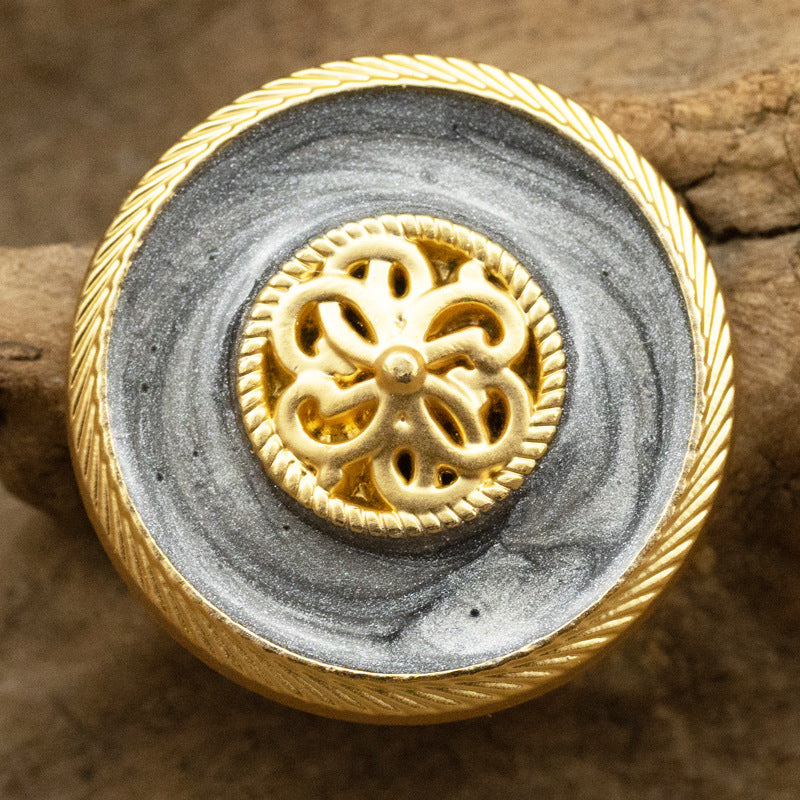 Pearl-glaze shank button in gray with ornate gold filigree center and ridged rim