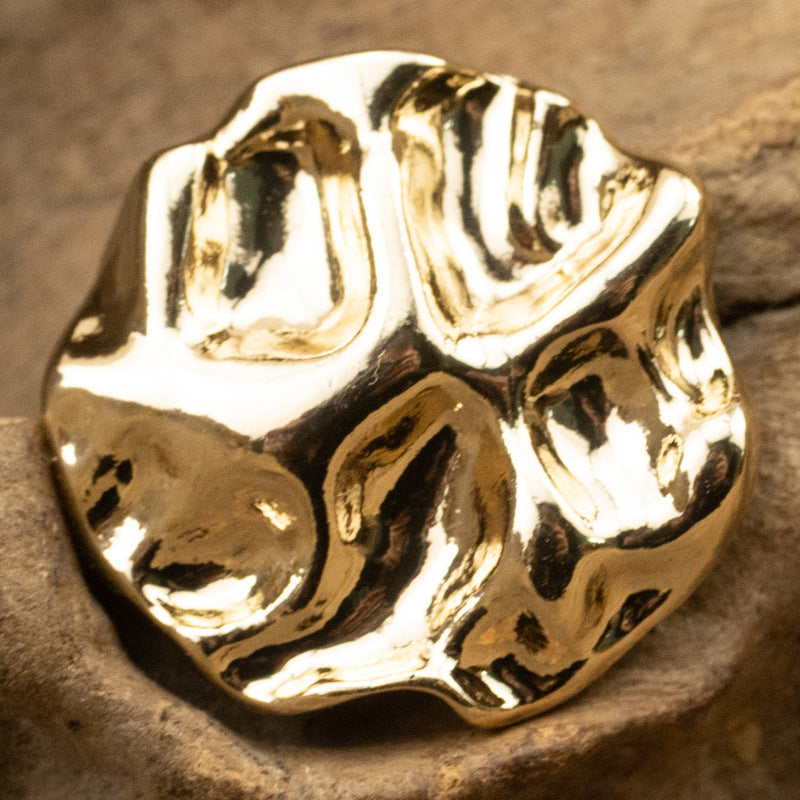 Gold metal button with irregular wave-pattern surface and shank, close-up