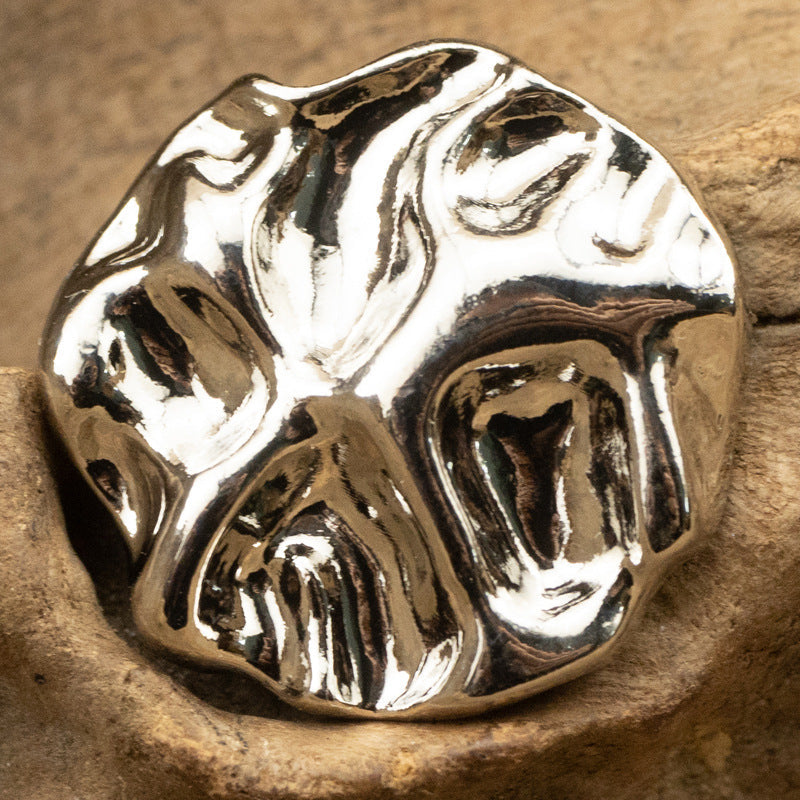 Silver metal button with irregular wave-pattern surface and shank, close-up