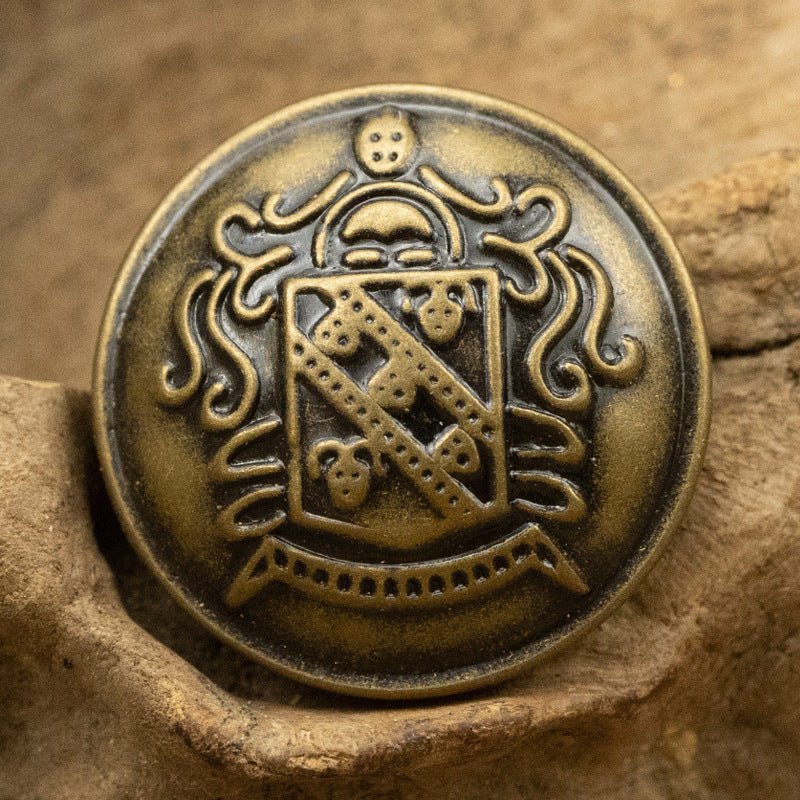 Round antique bronze brass button with shield emblem and decorative scrollwork