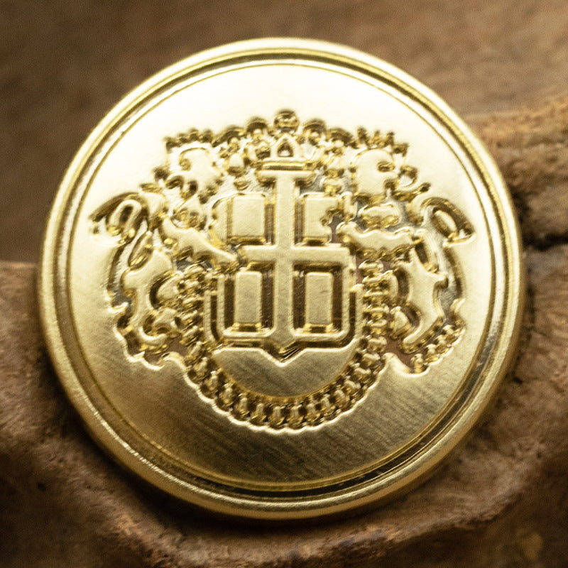 Golden shield metal button with crest/crown monogram and scalloped rim, close-up