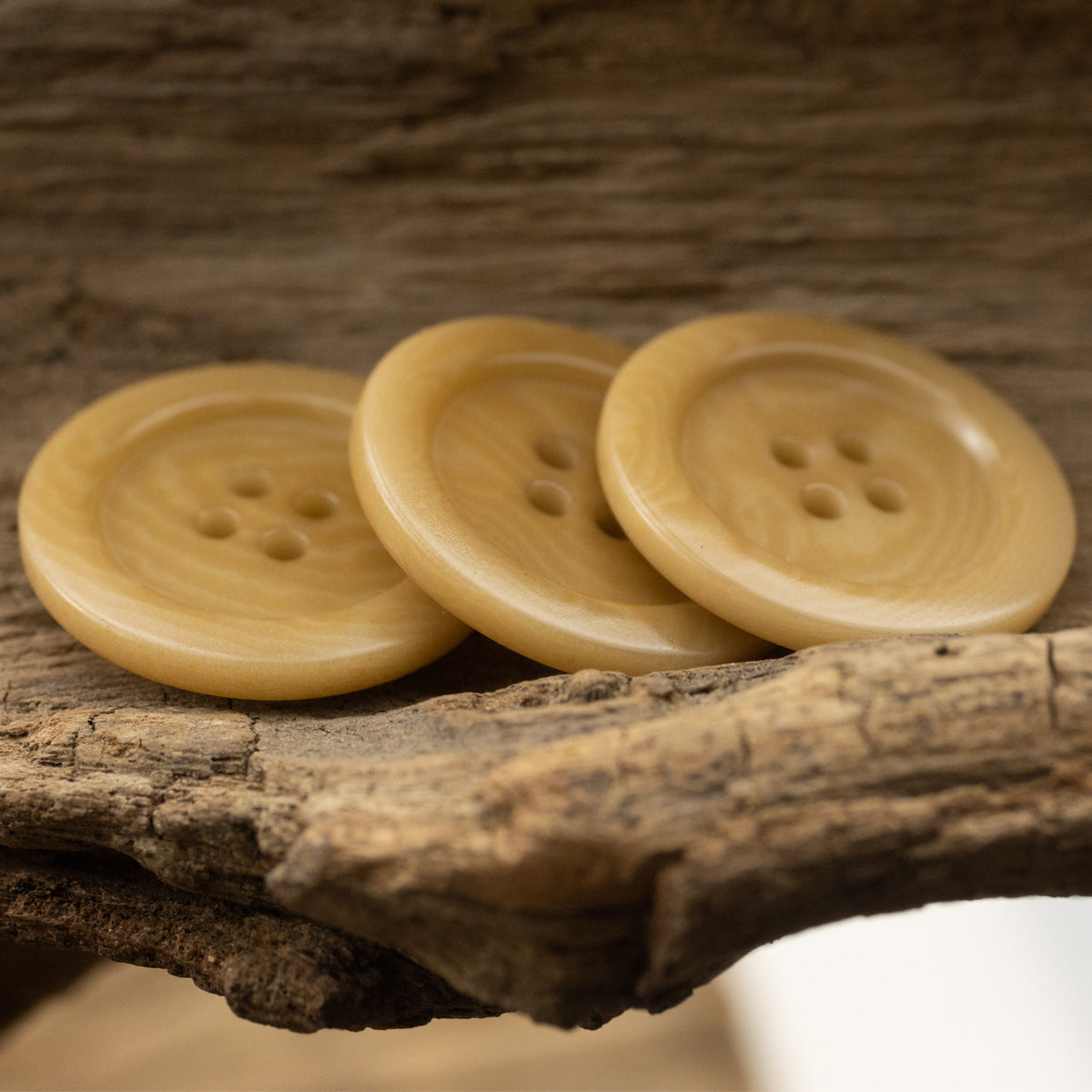 Set of three light yellow 4-hole sweater buttons, textured round front