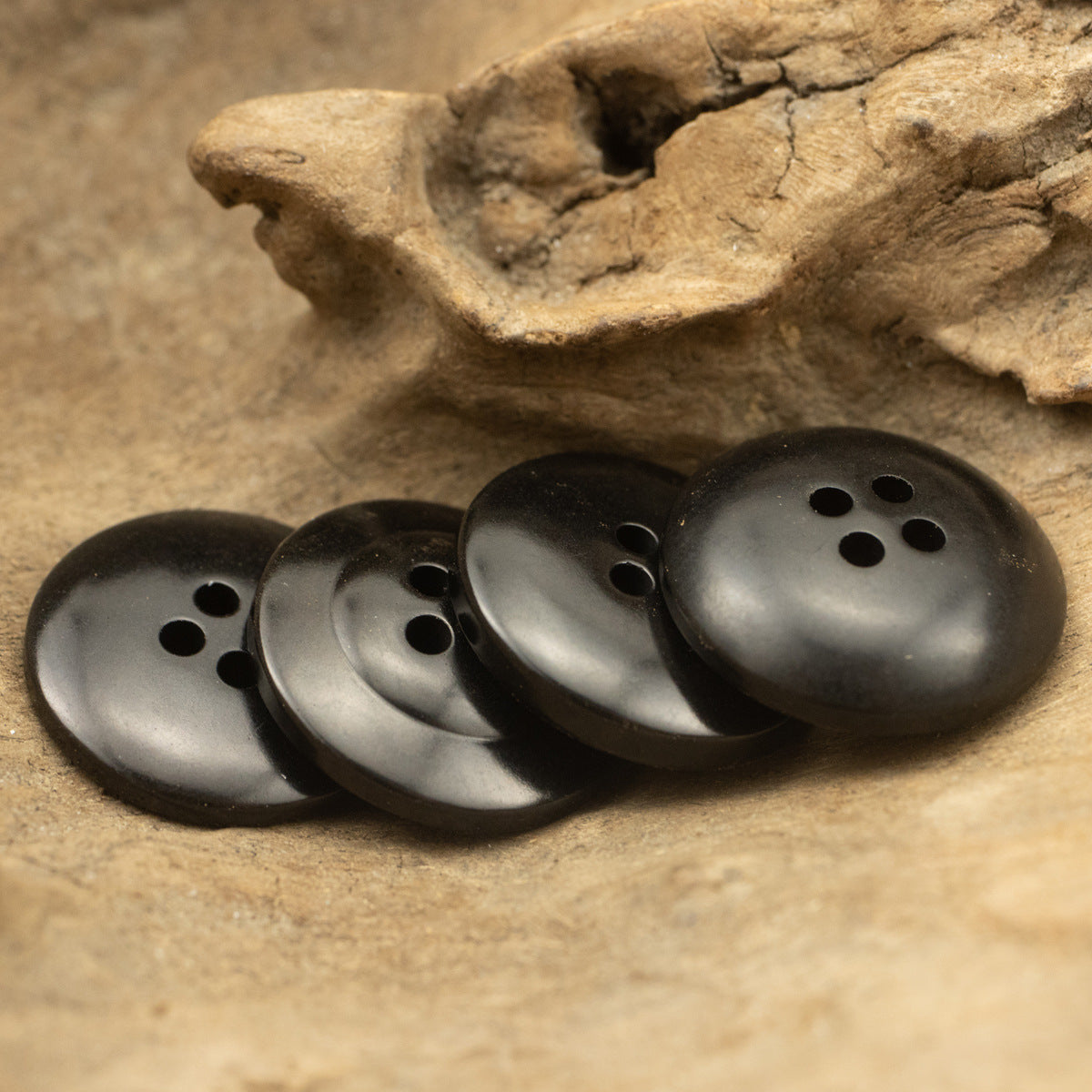 Black round suit buttons with 4 holes, several pieces on stone surface