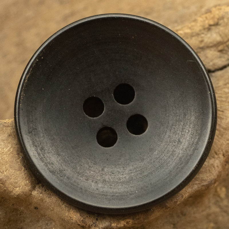 Black round button close-up, four holes and raised rim detail