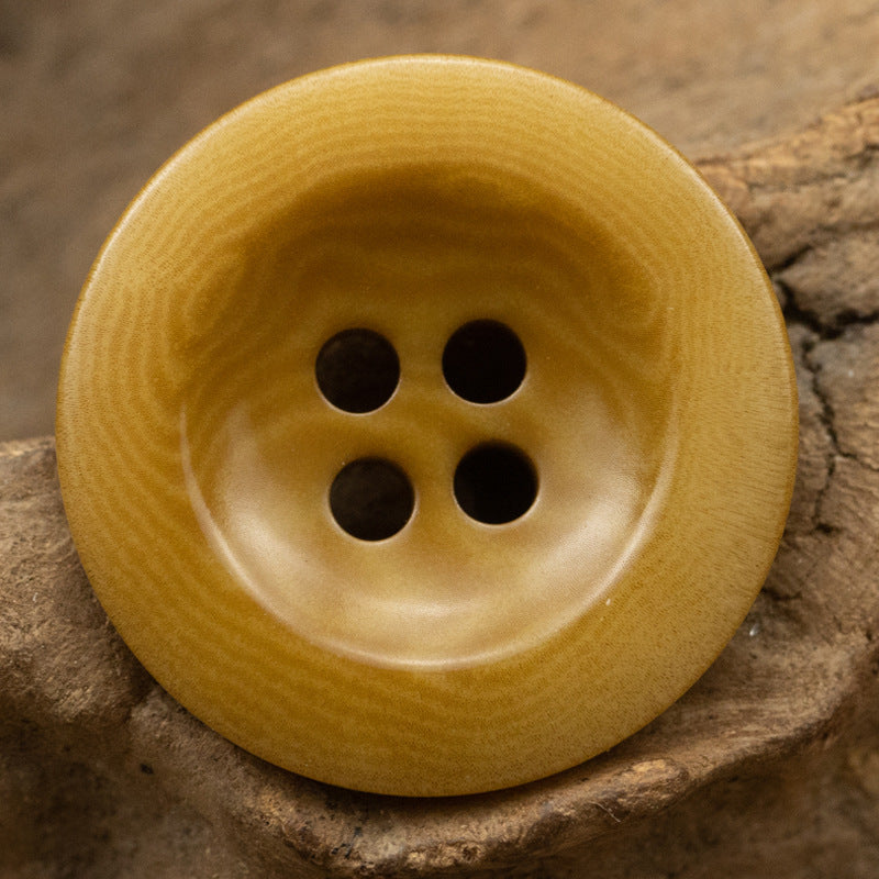 Khaki yellow 4-hole button, matte woodgrain surface with dark stitch holes