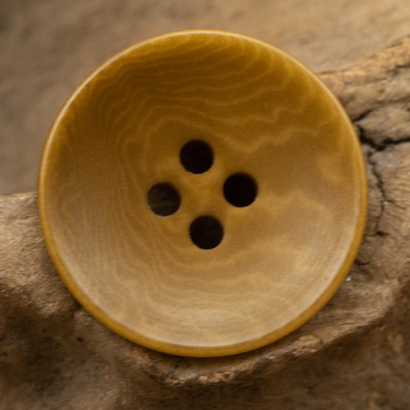 Khaki yellow 4-hole button, lighter underside, round shape with woodgrain pattern