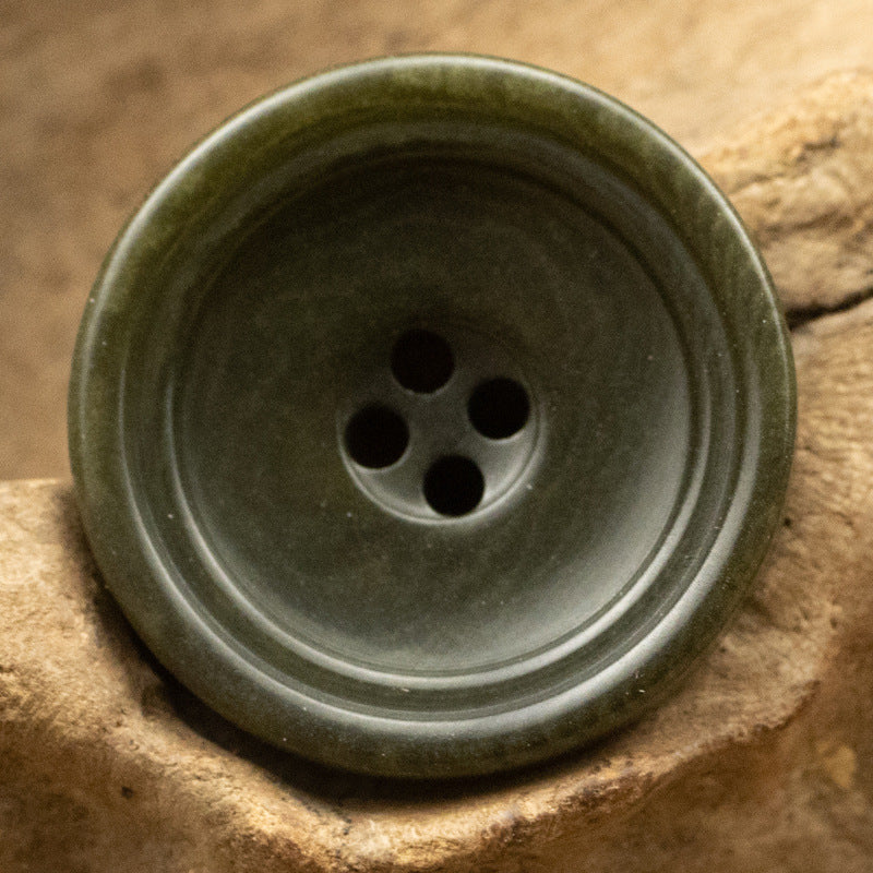 Army green round trouser button with 4-hole center and subtle striated pattern