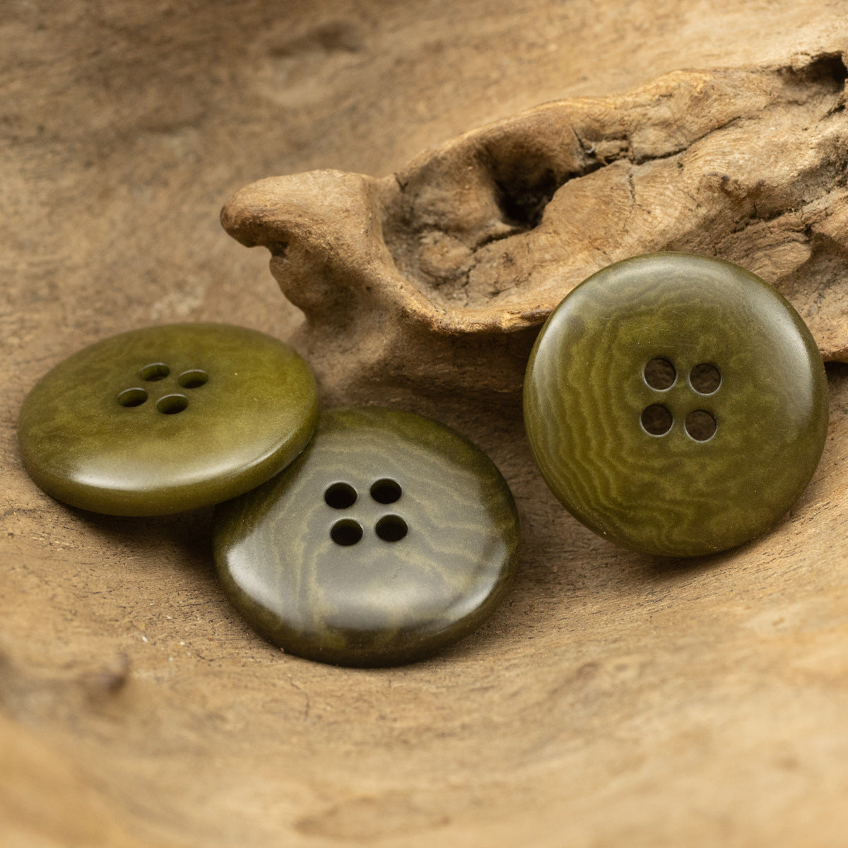 Three military green wide-edged four-hole fruit buttons with dark holes