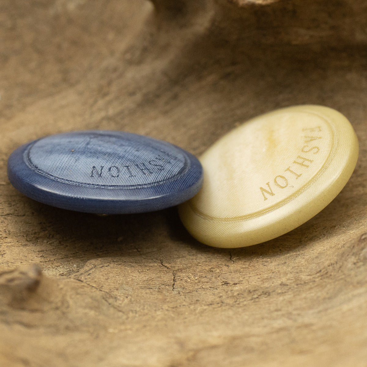 Light-yellow button with metal shank, paired with navy-blue button on wood texture