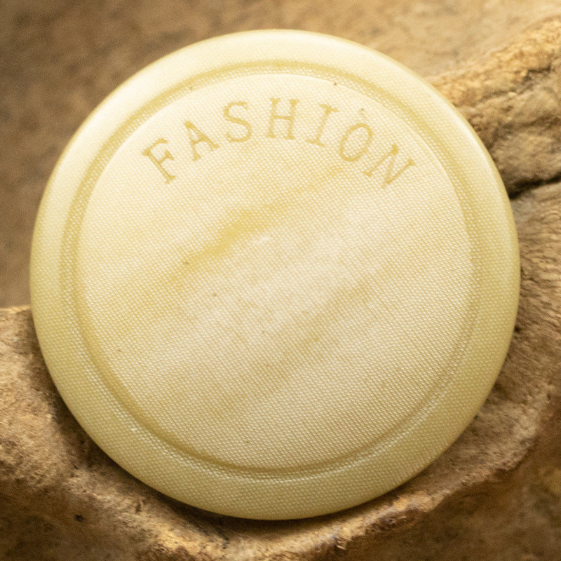 Light-yellow round button with 'FASHION' lettering on the back