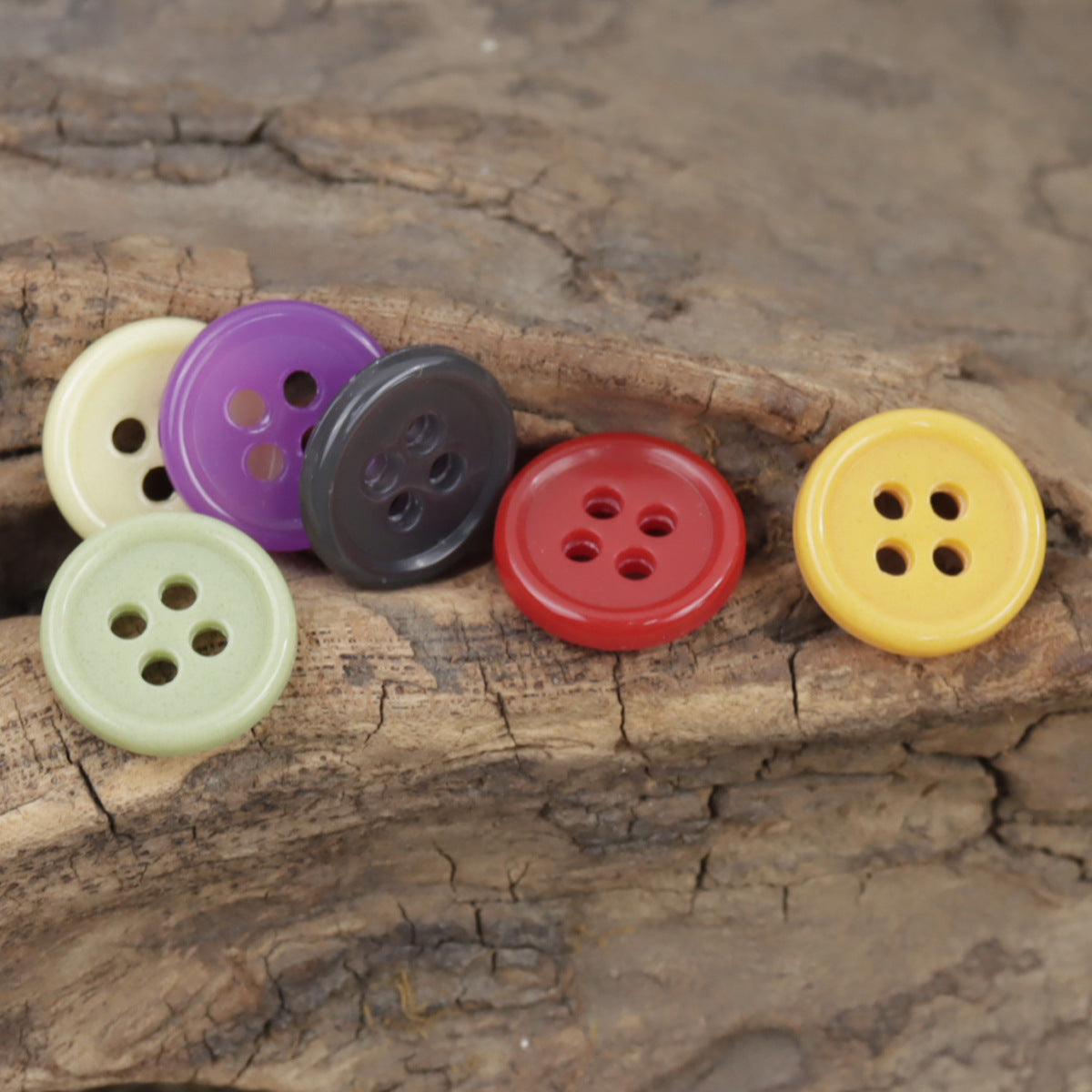 Five colorful 4-hole urea buttons on wood: cream, purple, gray, red, yellow