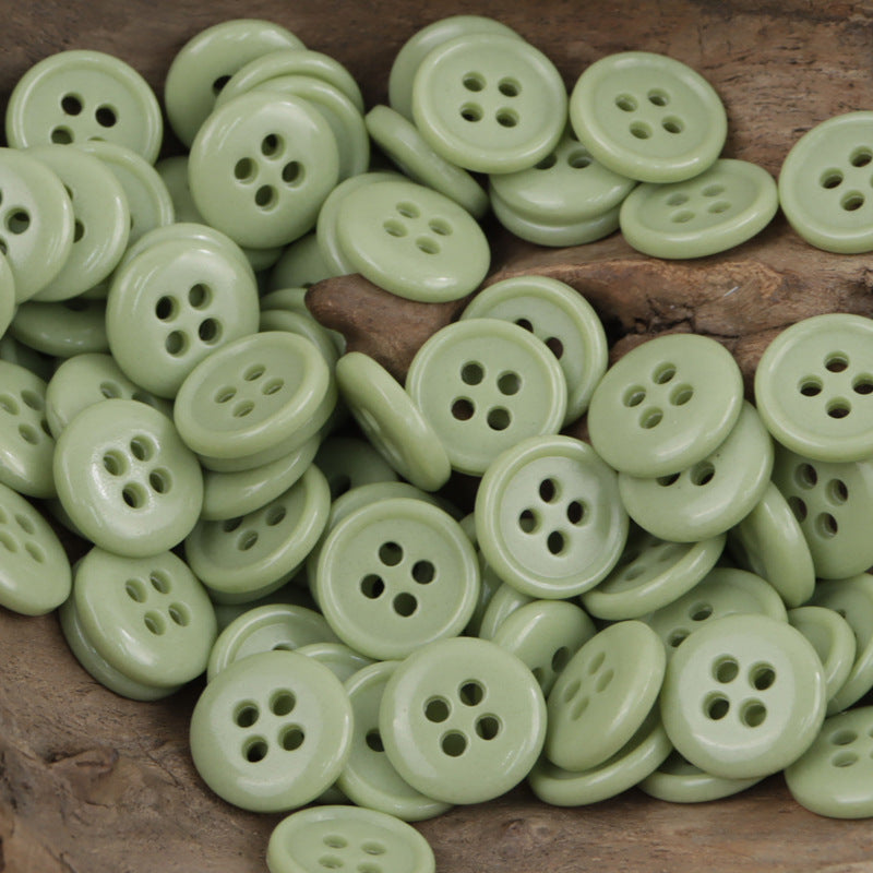 Light green 4-hole urea buttons, many round fronts on wood surface