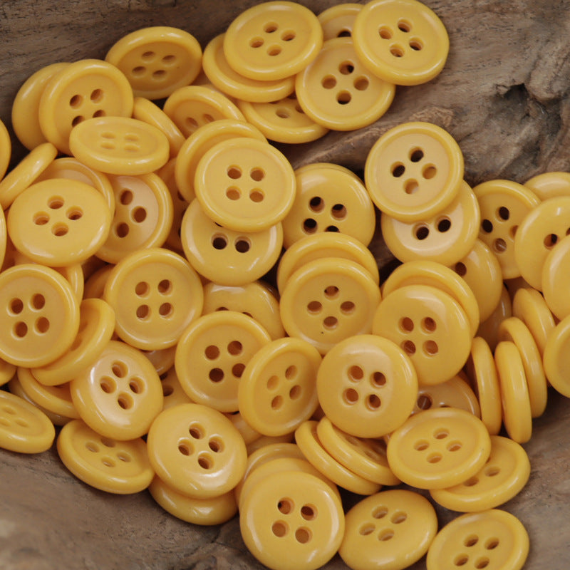 Yellow 4-hole urea buttons, many round fronts on wood surface
