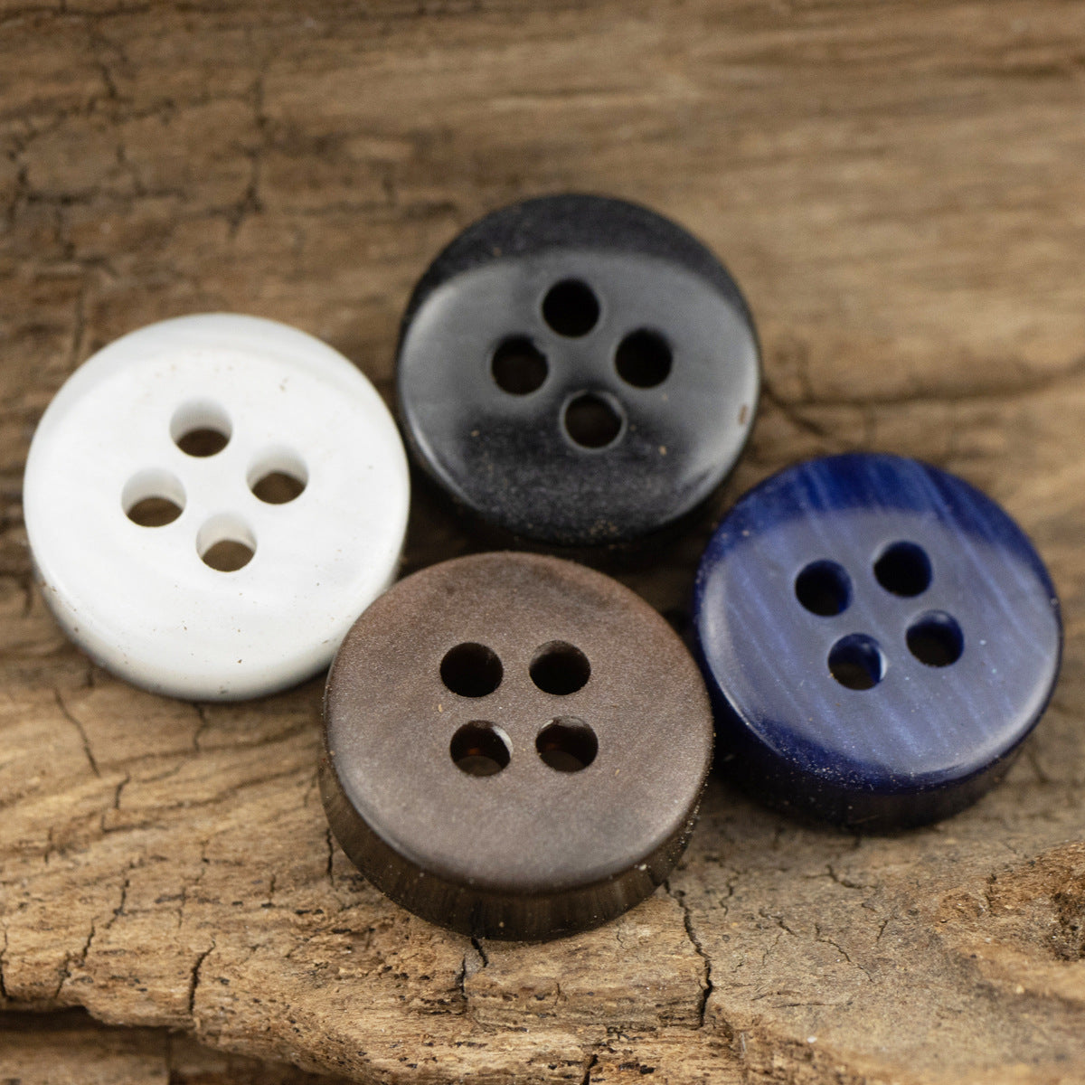 Resin 4-hole shirt buttons in white, dark gray, brown, and dark blue on a wood surface