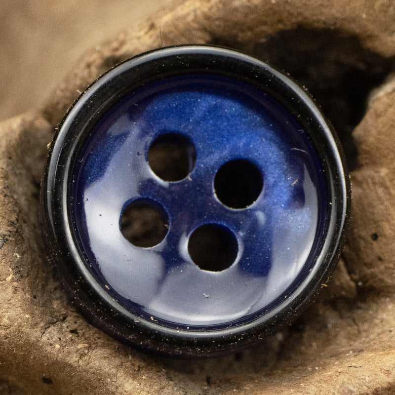 Close-up of dark blue 4-hole resin shirt button with black edging