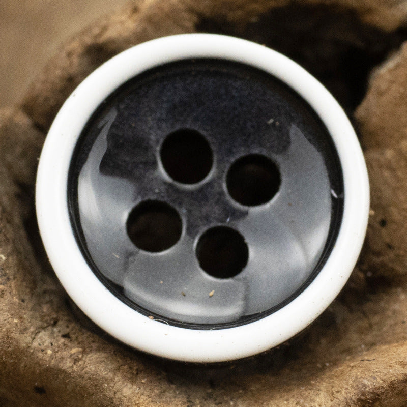 Close-up black/gray 4-hole resin shirt button with white rim and black edging