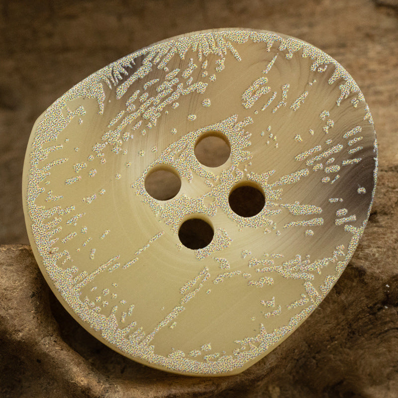 Cream resin button close-up with four holes and distressed frosted floral pattern