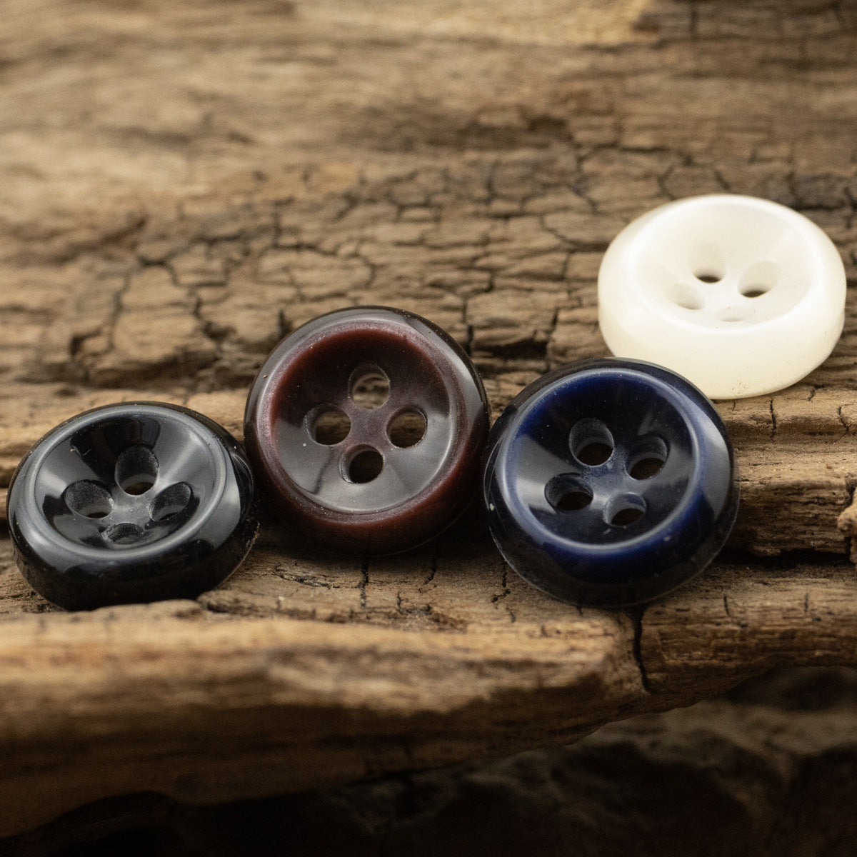 Mixed set of resin buttons: white, black, dark blue, and wine brown on wooden surface