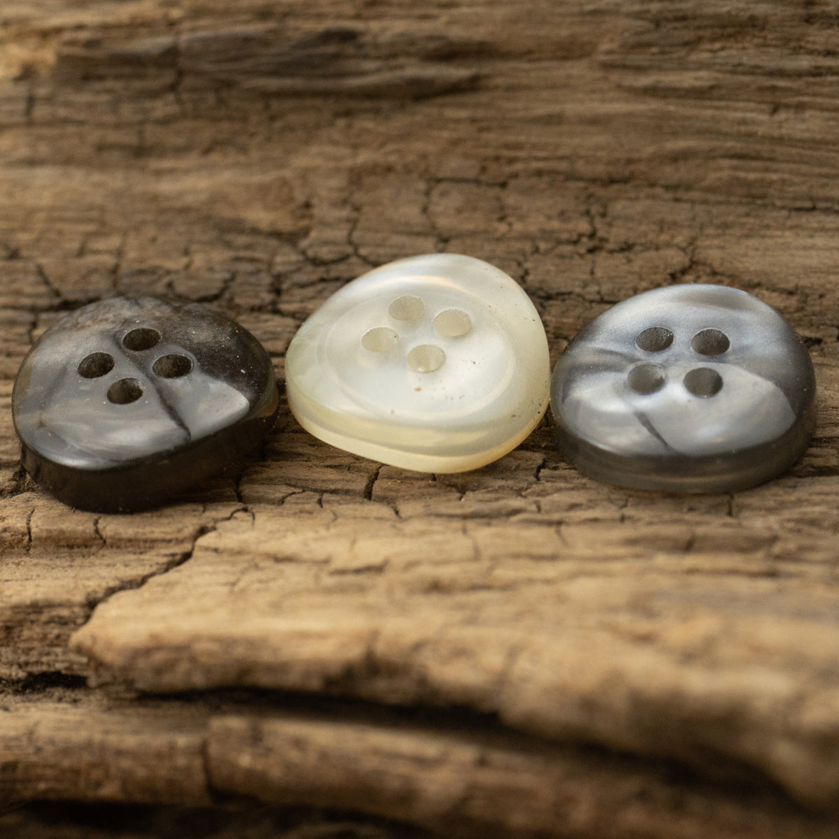 Three translucent glazed pearl resin buttons on wood: dark brown, khaki, gray, four holes