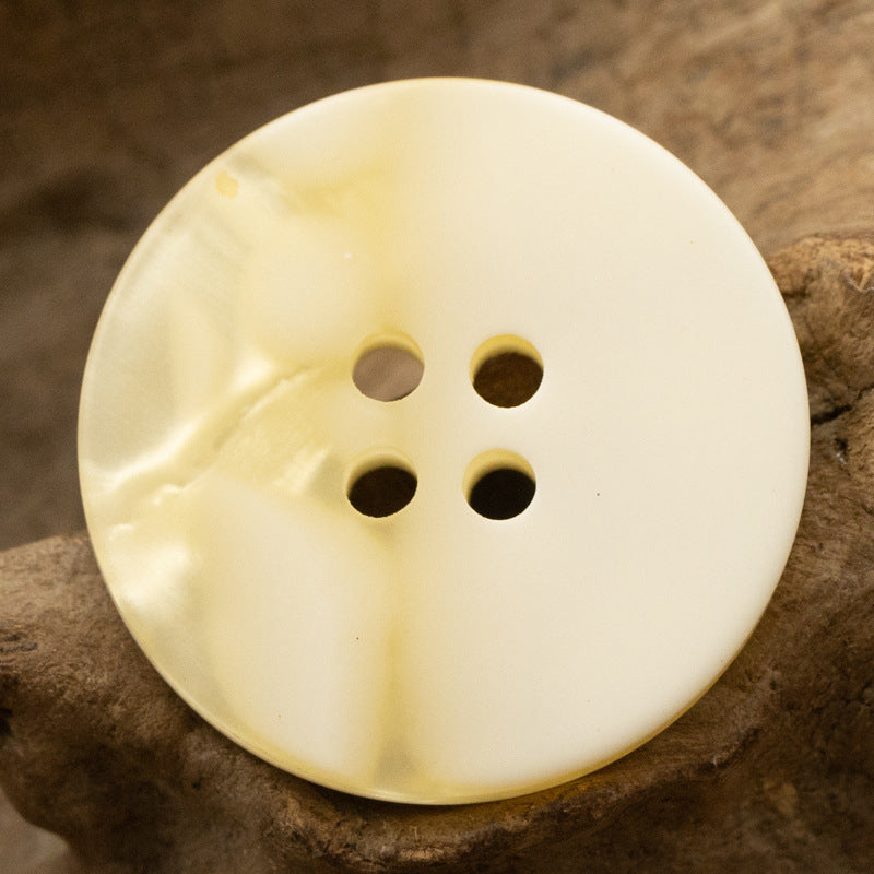 Cream/ivory round resin button with four holes for shirts and coats.