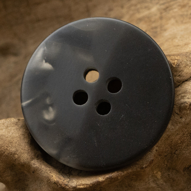 Black round resin button with four holes for shirts and coats.