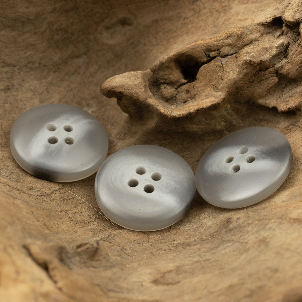 Three light gray round resin buttons with four holes, top view.