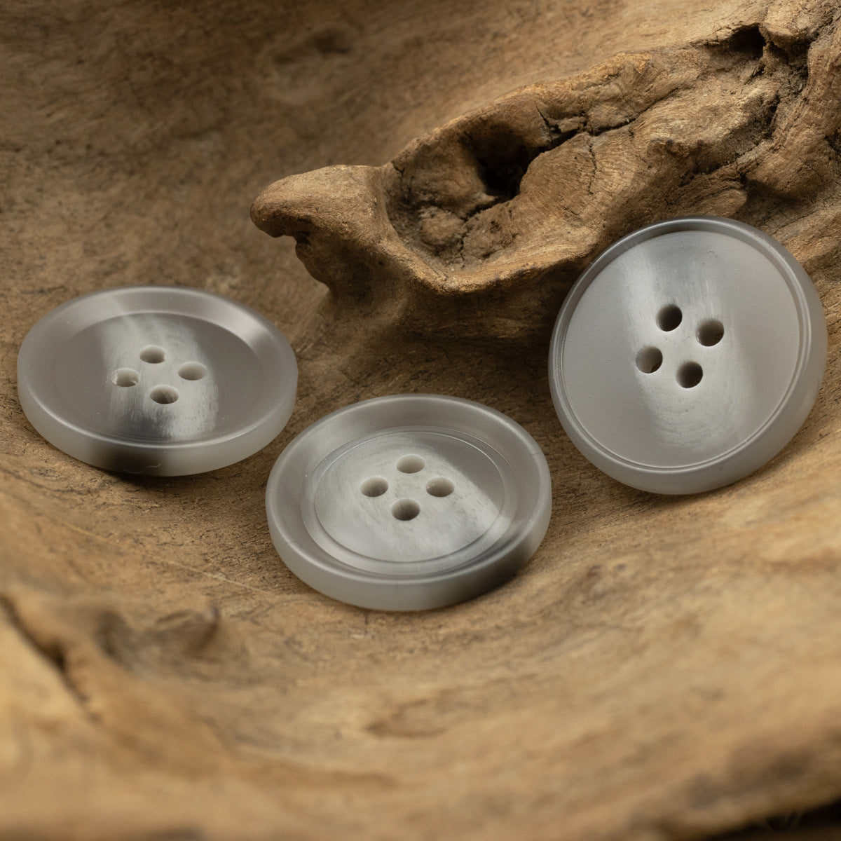 Three light gray round 4-hole resin buttons, top view.