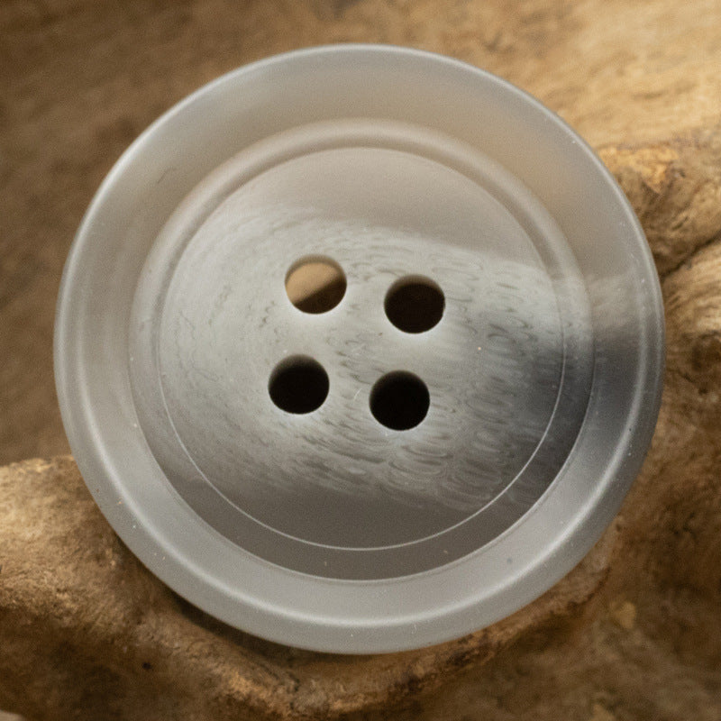 Light gray round resin button with four holes, close-up front.