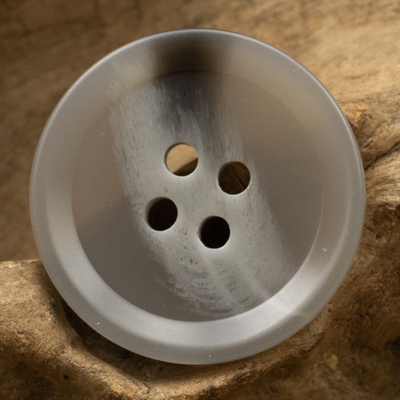 Light gray round 4-hole resin button, textured surface, front close-up.