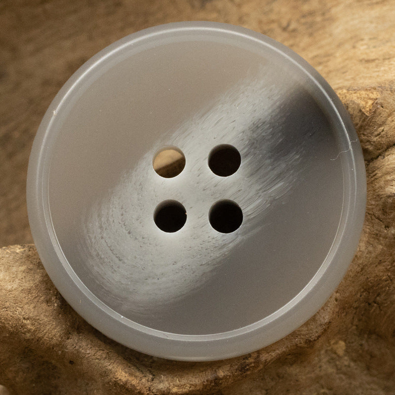 Light gray round resin button with four holes, angled close-up.