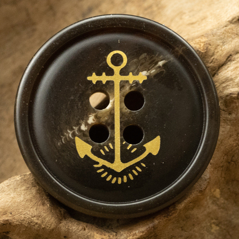 Black/dark resin anchor button with gold sailor anchor motif, 4-hole front view
