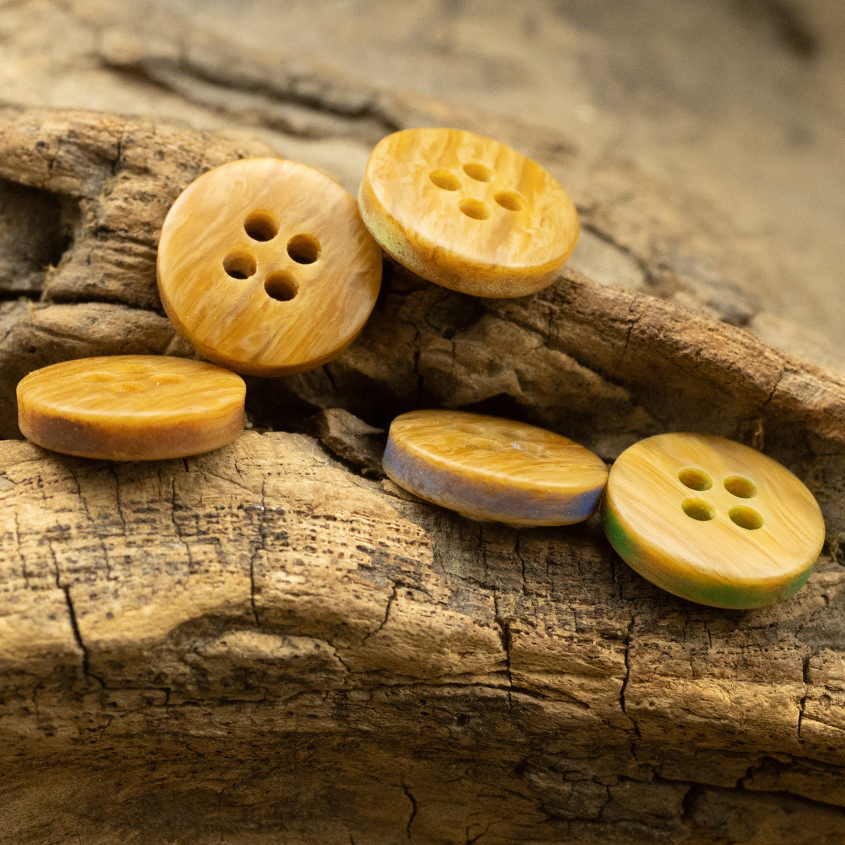 Woodgrain-style resin buttons with four holes in yellow and green tones, on a rustic surface.