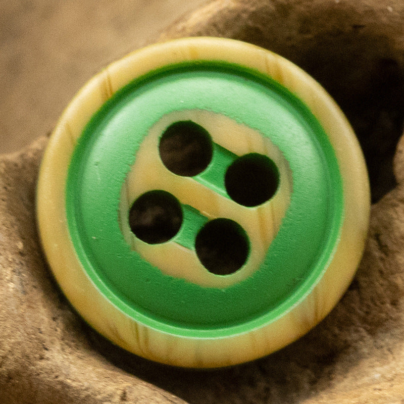 Green-and-yellow four-hole resin button with dark holes and woodgrain rim.