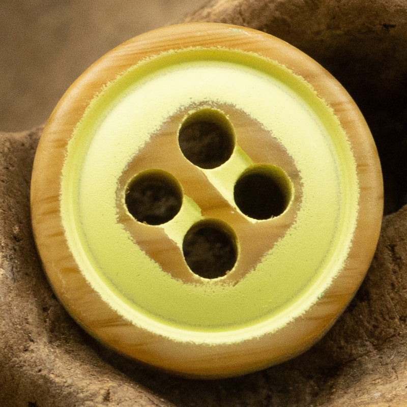 Lemon-yellow four-hole resin button with dark holes and warm woodgrain border.