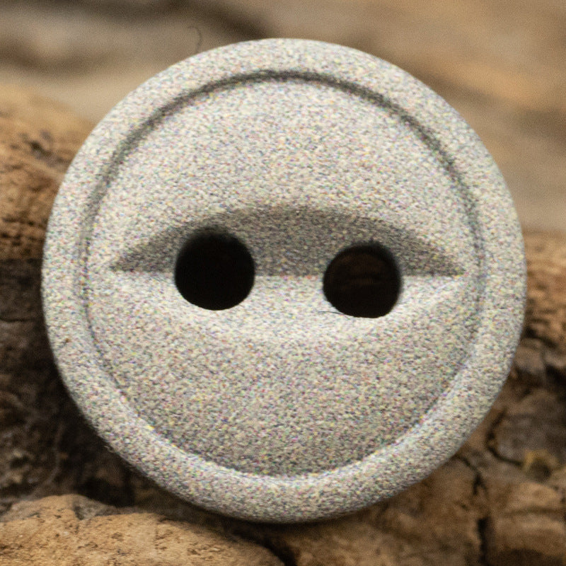 Gray speckled resin button close-up, round with two holes and textured edge