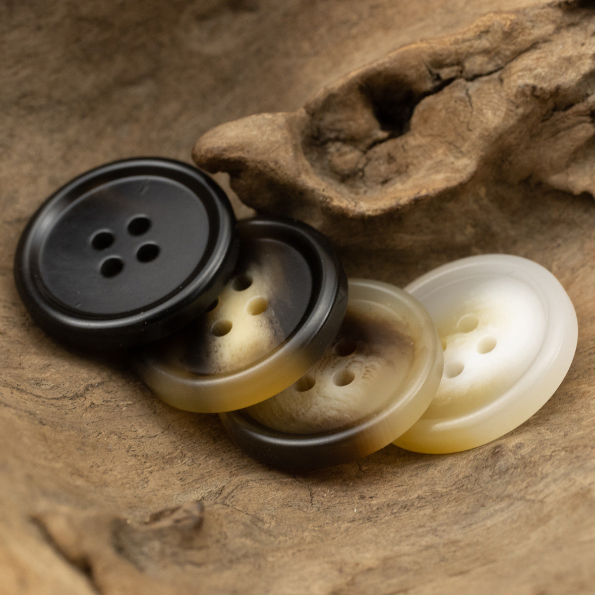 Four-hole resin buttons in black, smoky brown, tan, and cream hues (set shown)