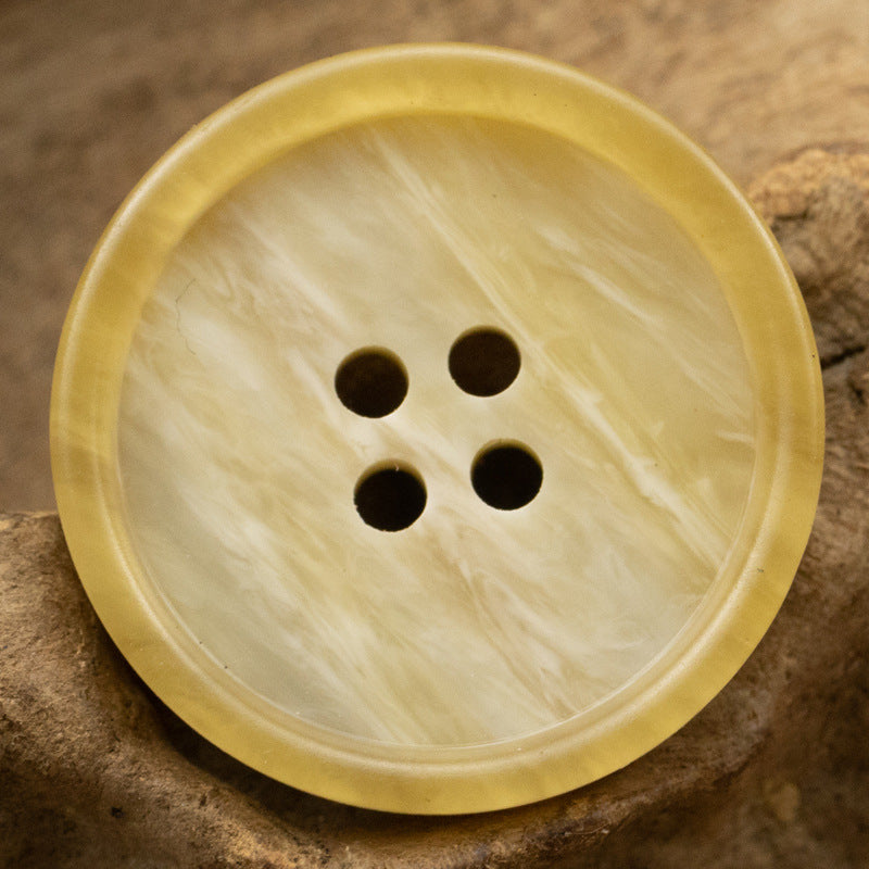 Light yellow round resin button with 4 holes and subtle marbled grain