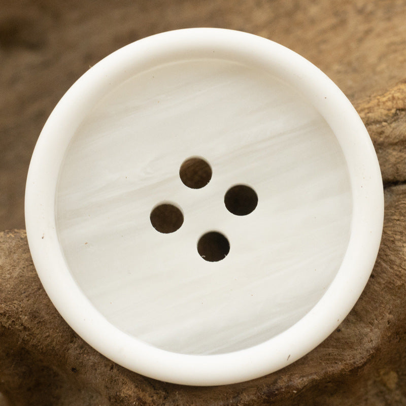 White round resin button with 4 holes and faint marbled grain